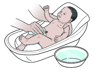 Hand mit Tuch, das ein neugeborenes Kind in einer Babybadewanne wäscht, eine Schüssel mit Wasser in der Nähe.